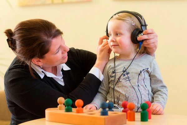 Eine Logopädin testet das Hörvermögen eines Mädchens mit Kopfhörern im Therapieraum.