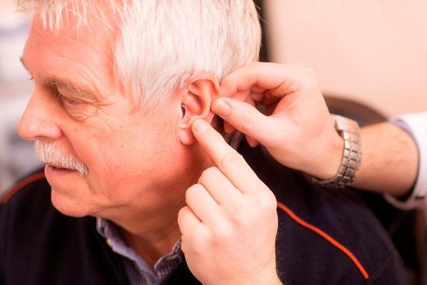 Ein älterer Mann erhält die Anpassung eines modernen Hörgeräts im Ohr.
