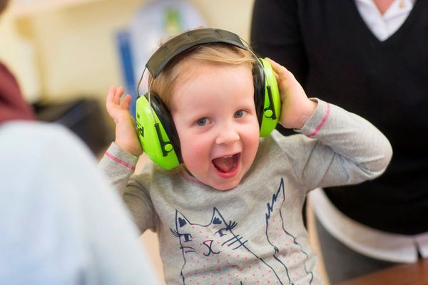 Fröhliches Kind mit Lärmschutzkopfhörern und Katzenpullover in einer Kita.